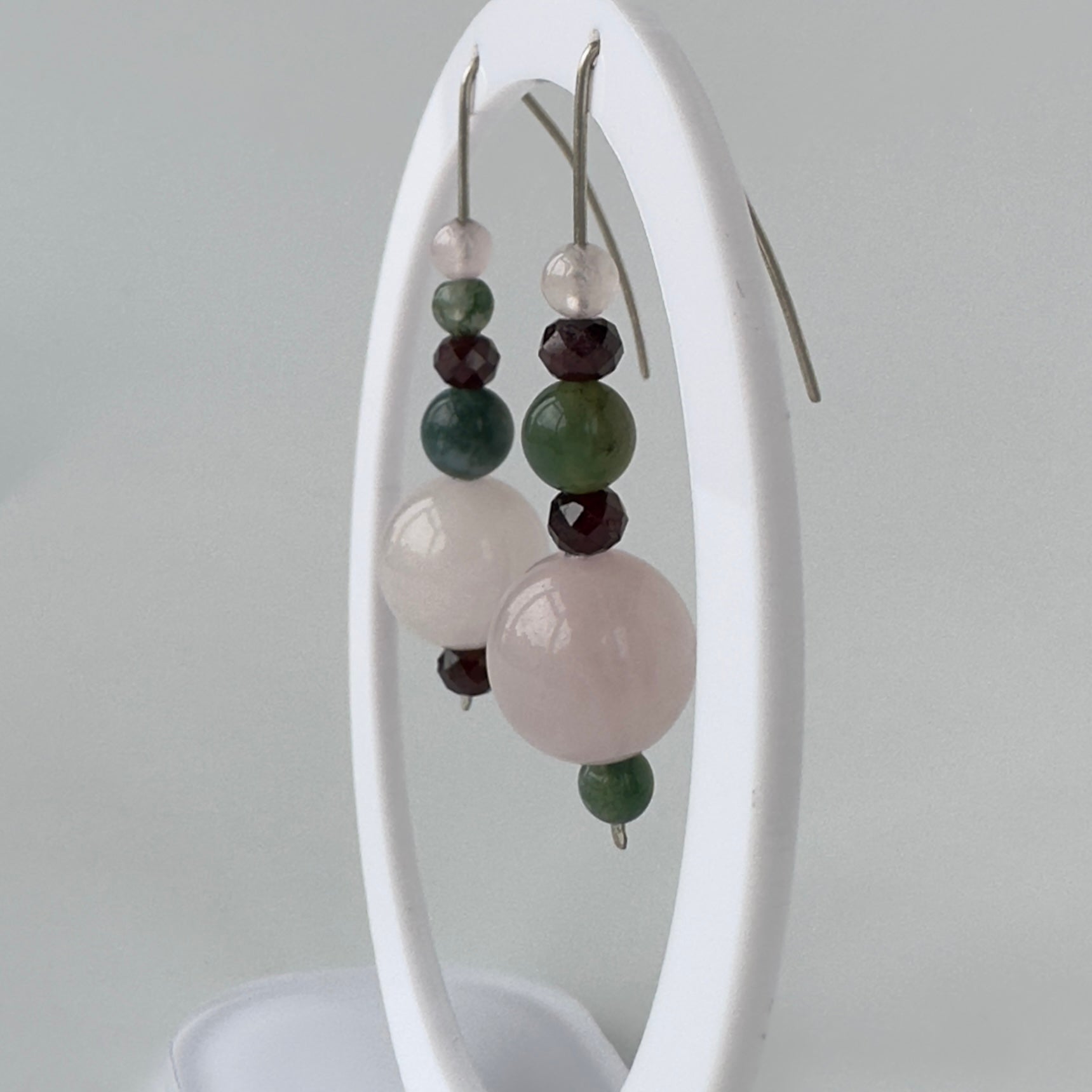 Earrings with multicolored beads on a white stand against a gray background
