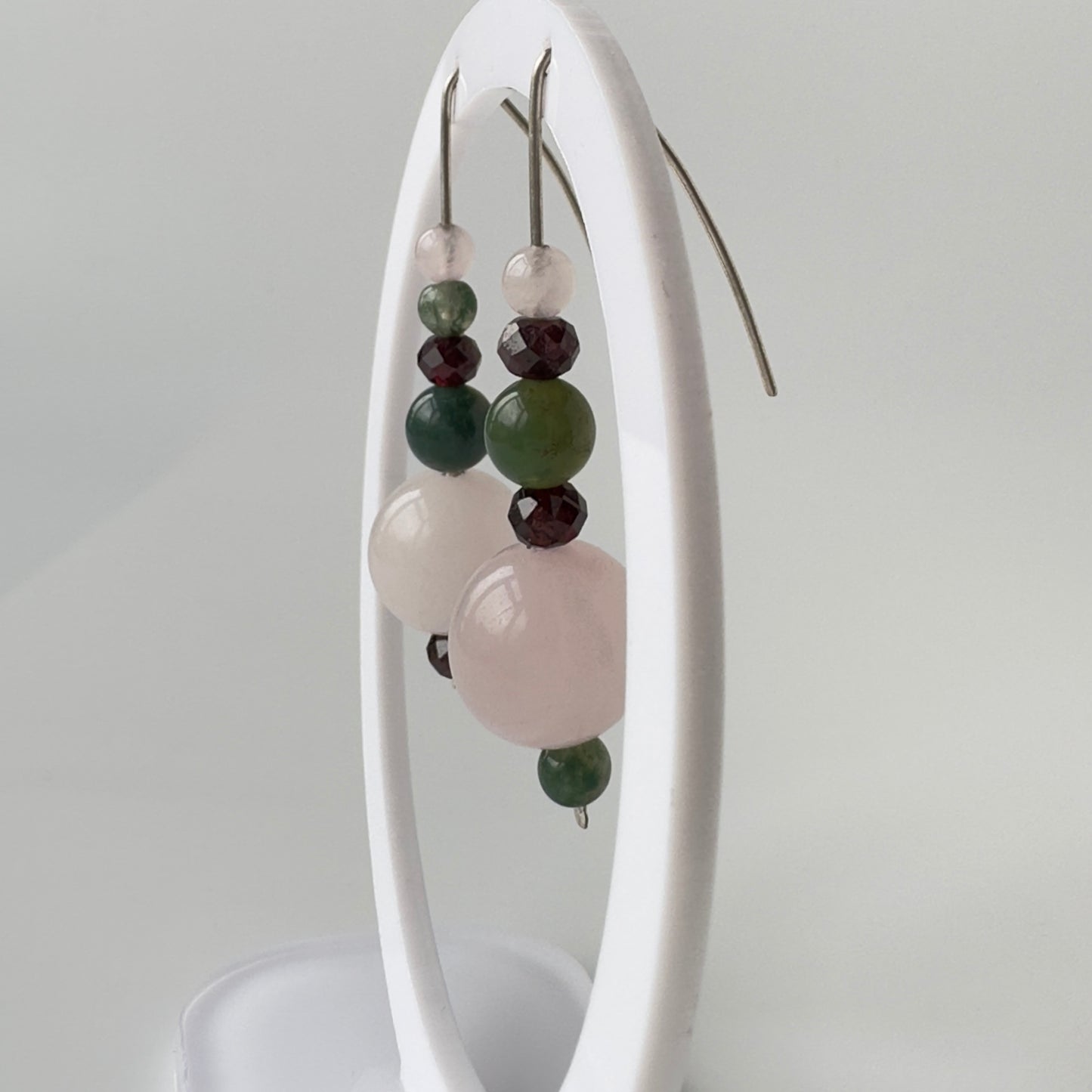 Earrings with multicolored beads on a white stand against a light gray background
