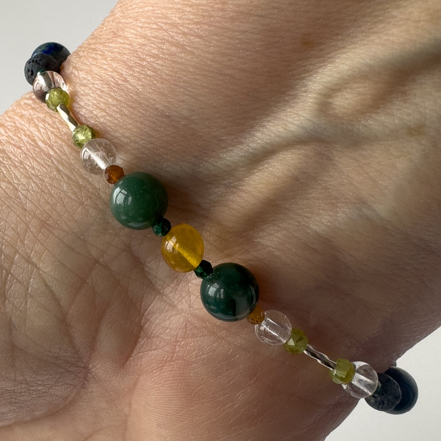 Capricorn Birthstone Healing Crystal bracelet for Love and Compassion on wrist showing Peridot, Amber, Moss Agate, Azurite, Garnet, Malachite and Clear Quartz