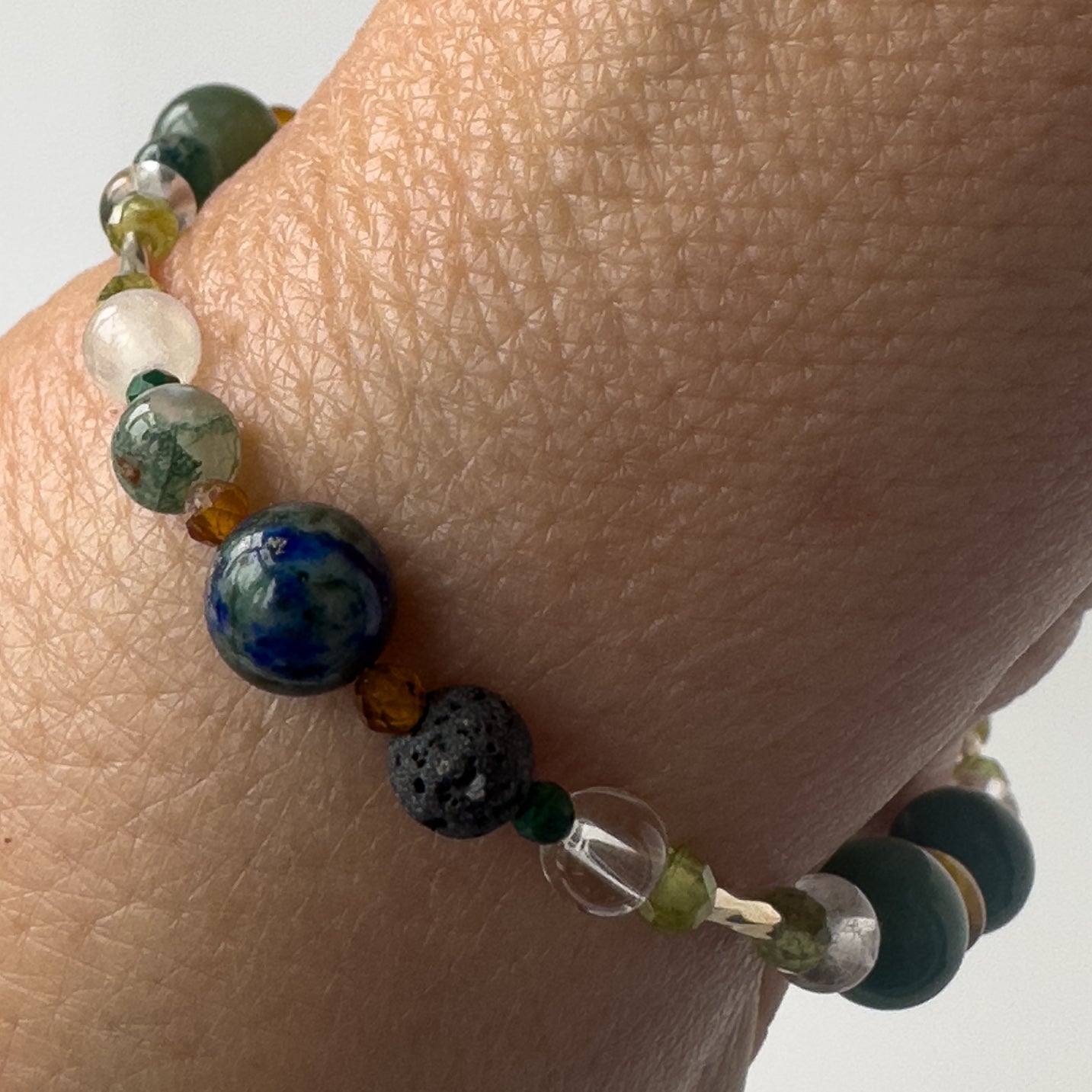 Capricorn Birthstone Healing Crystal bracelet for Love and Compassion on wrist showing Peridot, Moss Agate, Azurite, Garnet, Malachite, Lava Stone, Selenite and Clear Quartz