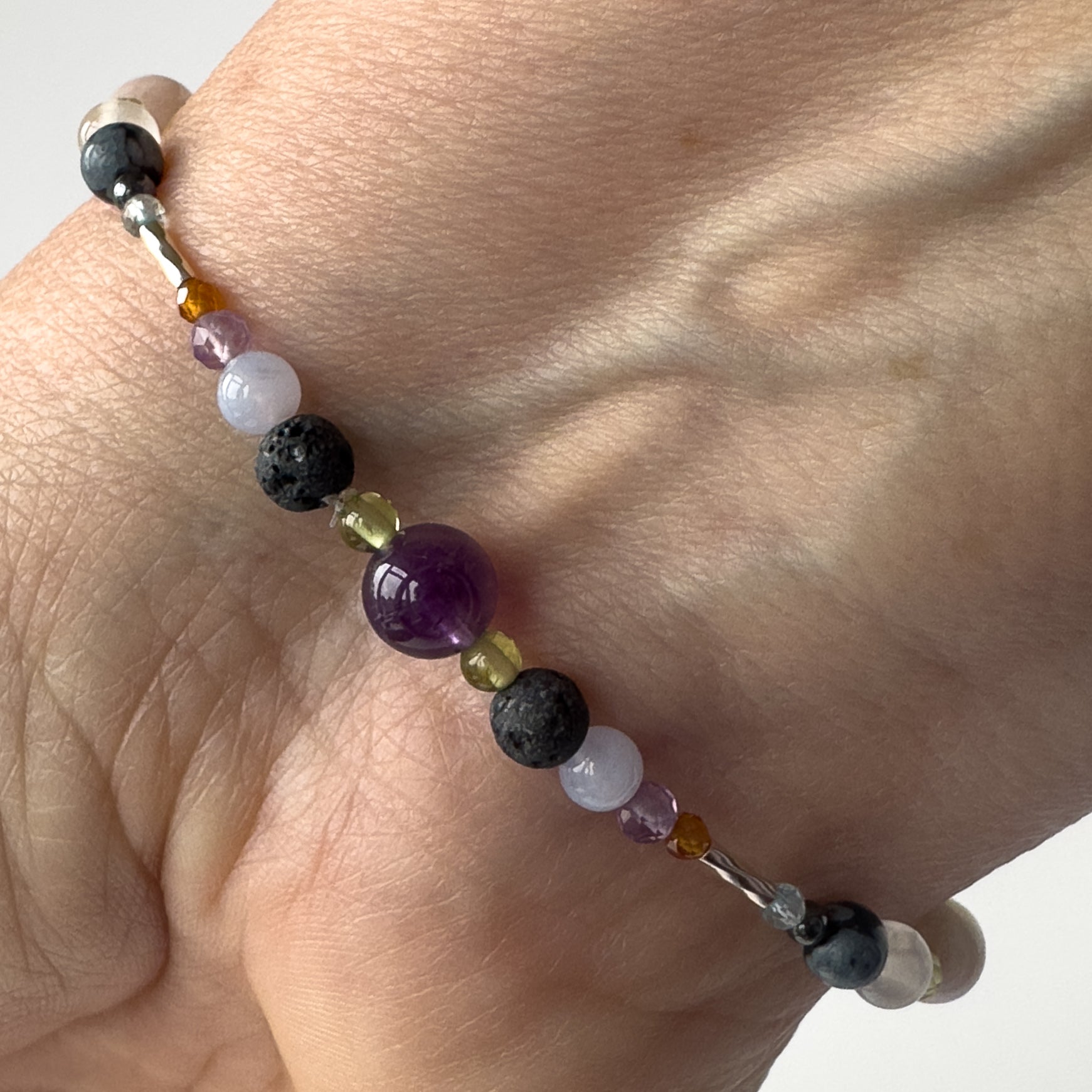 Close-up of Scorpio birthstone Healing crystal bracelet for Calm & Stress on wrist showing Peridot, Blue Lace Agate, Amethyst, Garnet and Lava Stone