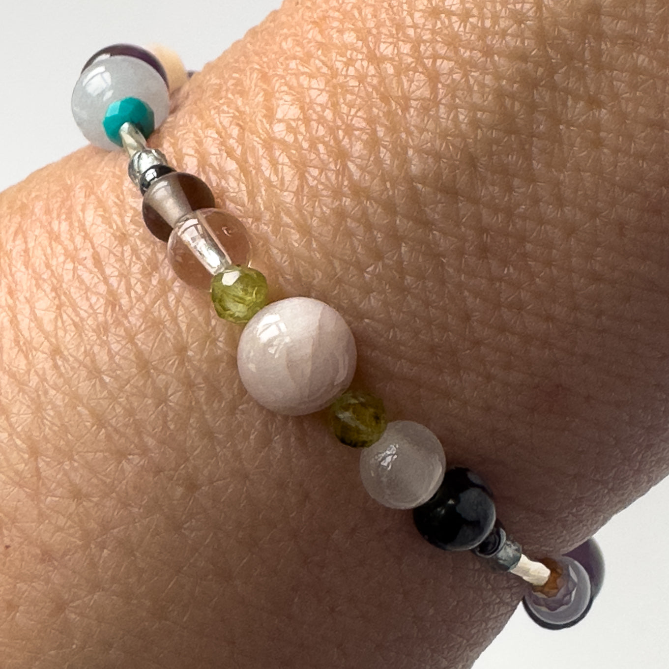 Scorpio birthstone Healing Crystal bracelet for Calm & Stress on wrist showing Smoky Quartz, Peridot Snowflake Obsidian, Kunzite, Selenite and Clear Quartz