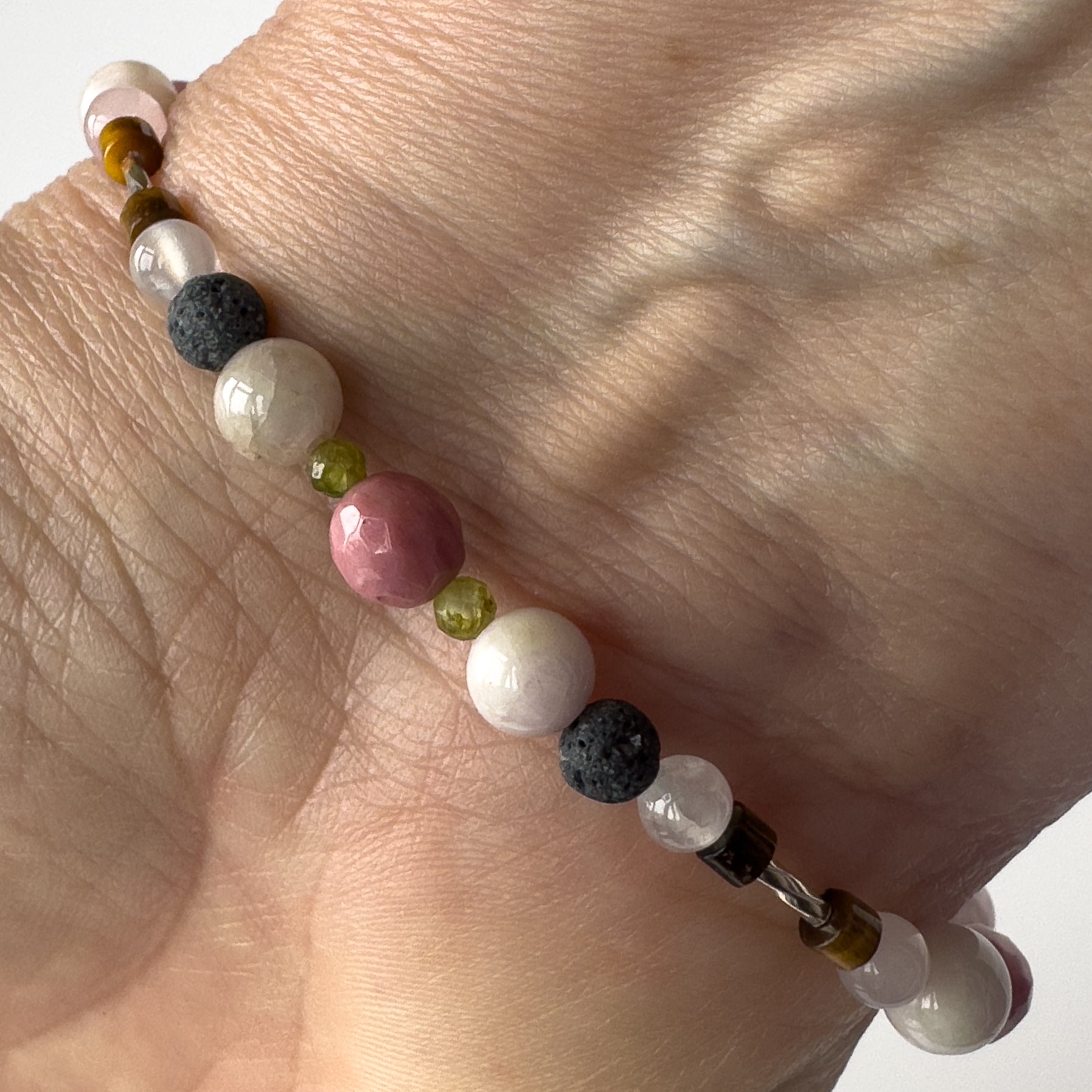 Taurus Birthstone Healing Crystal bracelet for Love and Compassion on wrist showing Peridot, Kunzite, Rhodonite, Tiger’s Eye, Lava Stone and Clear Quartz