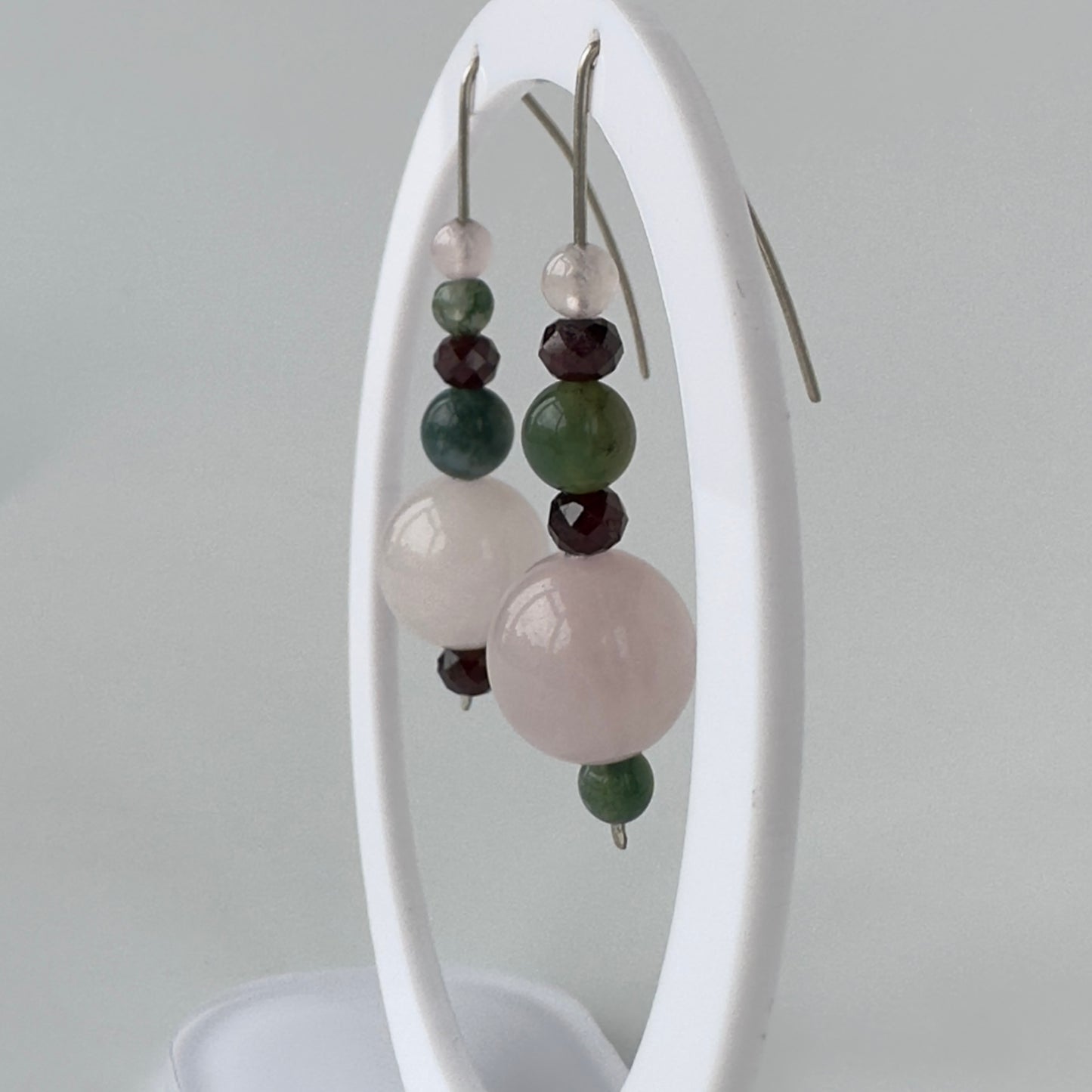 Earrings with multicolored beads on a white stand against a gray background