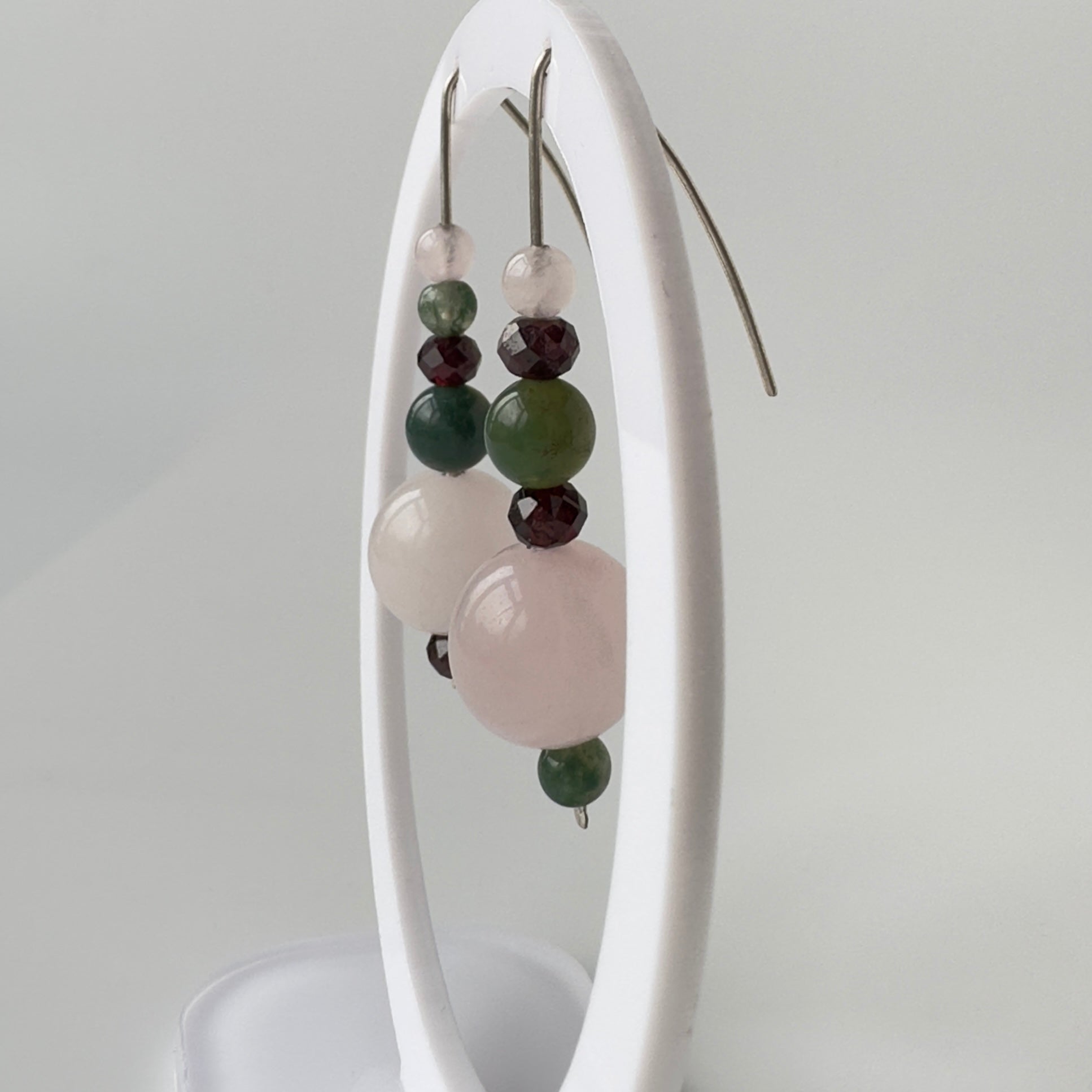 Earrings with multicolored beads on a white stand against a light gray background