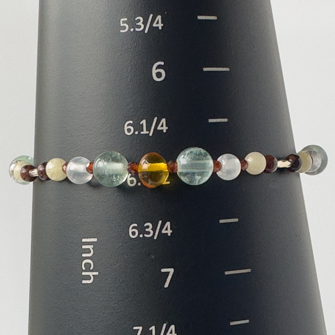 Capricorn Healing Crystal bracelet for Confidence on wrist showing Garnet, Mahogany Obsidian, Amber, Fluorite and Aragonite on mandrel showing a size of 6.5 inches