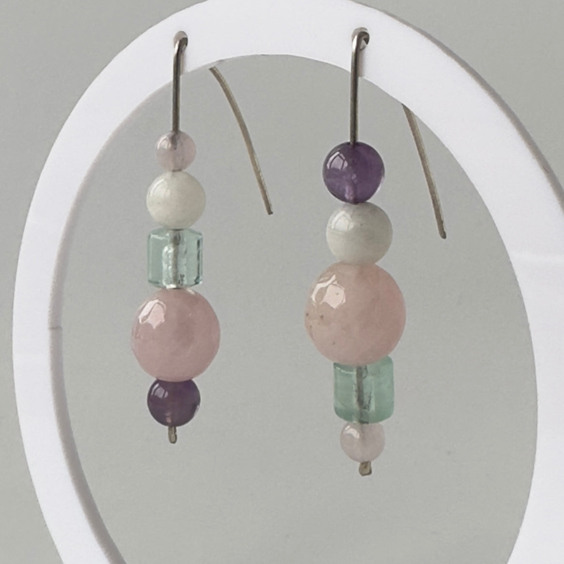 Beaded earrings with pink, green, and purple beads on a white circular stand.