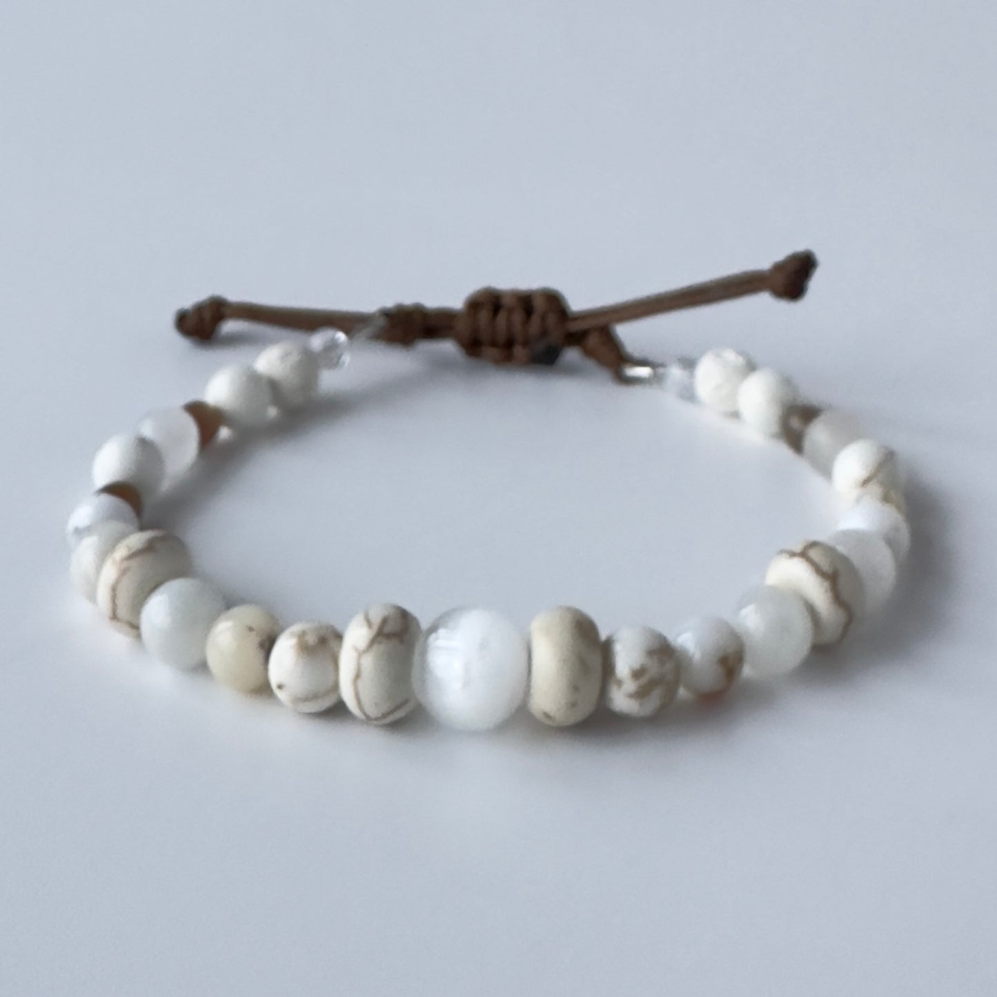 Bracelet with white beads and brown nylon strap on a light gray background