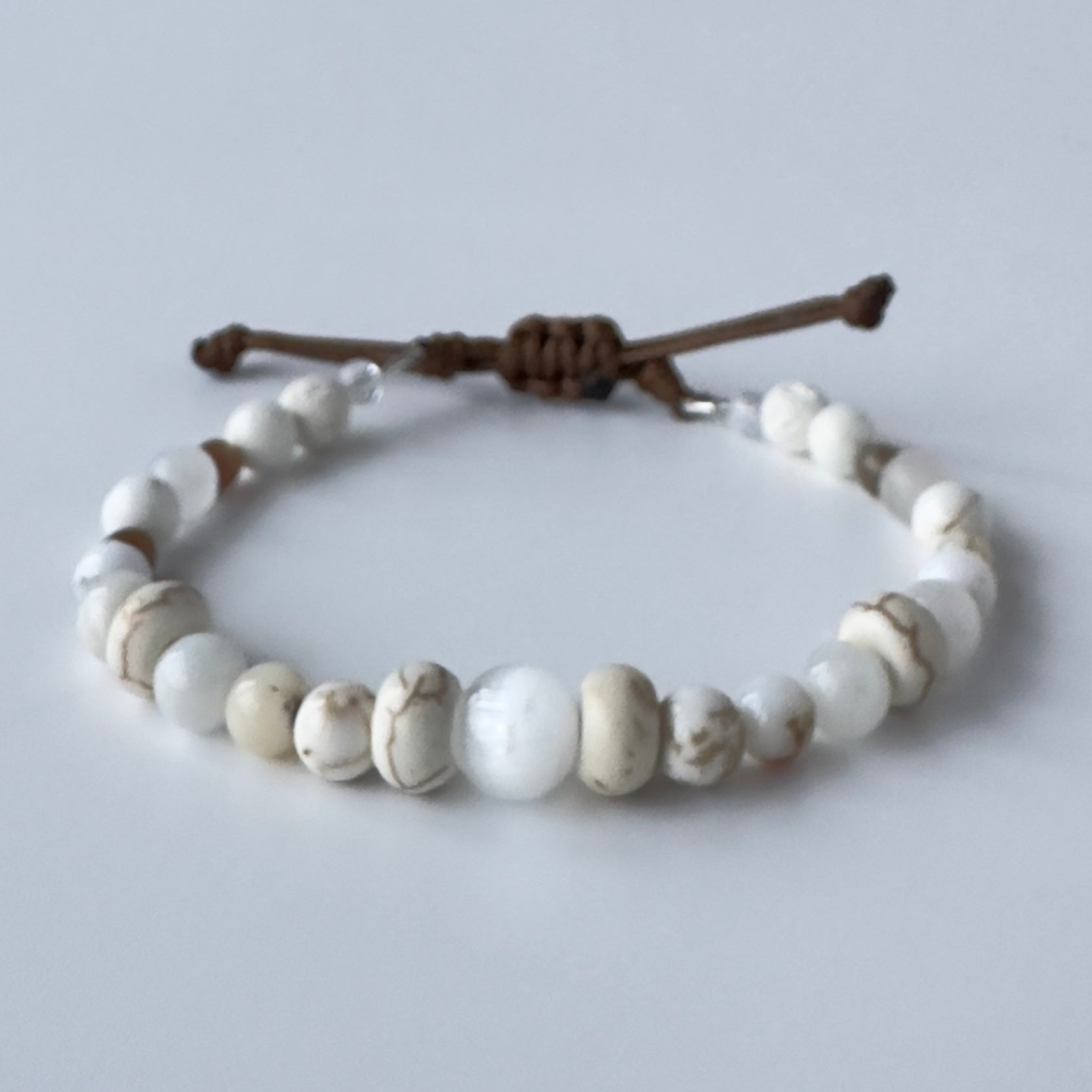 Bracelet with white beads and brown nylon strap on a light gray background